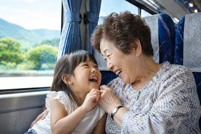 貸切バスの車内で祖母と子どもが笑顔で過ごす家族旅行の様子