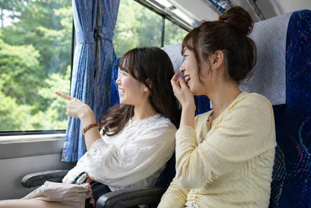 貸切バスの車内で会話を楽しむ友人同士の旅行シーン