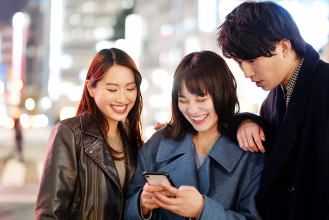 夜の街でスマホを見る3人のグループ